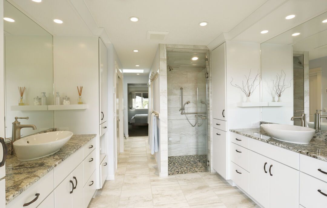 Bathroom with twin white vanities facing each other, granite countertops, vessel basins and a tiled walk-in shower